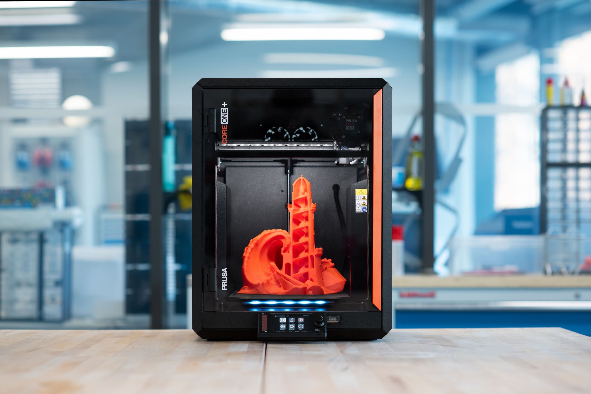 CORE One+ (Gen 2) printing an orange model in a workshop